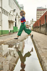 Junge Frau springt über eine Pfütze auf einer Straße - VEGF01808