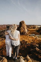 Rückansicht von Freundinnen mit Blick auf die Vulkanlandschaft im geothermischen Gebiet Dallol, Danakil-Senke, Äthiopien, Afar - LHPF01163