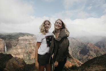 Portrait of happy friends standing against majestic mountains at Waimea Canyon State Park, Kauai, Hawaii, USA - LHPF01186