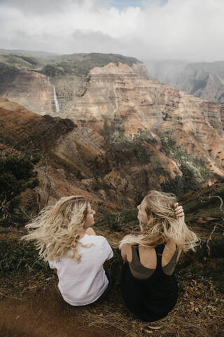 Rückansicht von Freunden, die sich unterhalten, während sie gemeinsam den Waimea Canyon in Kauai, Hawaii, USA, erkunden, lizenzfreies Stockfoto