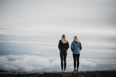Rückansicht von Freundinnen, die eine idyllische Wolkenlandschaft betrachten, während sie auf dem Vulkan Haleakala stehen, Hawaii, Maui, USA - LHPF01197