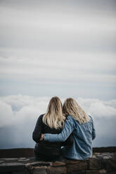 Rear view of female friends looking at idyllic cloudscape while sitting at Haleakala Volcano, Hawaii, Maui, USA - LHPF01198