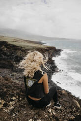 Rear view of woman with tousled hair sitting on cliff at USA, Hawaii, Maui - LHPF01199