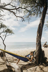 Junge Frau liest ein Buch und ruht sich in einer Hängematte am Strand aus, Maui, Hawaii, USA - LHPF01204