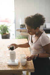 Woman working in a coffee roastery pouring coffee beans into a cup - JPIF00522