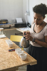 Woman working in a coffee roastery pouring hot water into coffee cups - JPIF00526