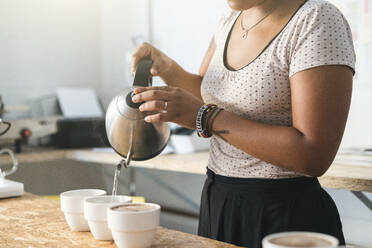 Nahaufnahme einer Frau, die in einer Kaffeerösterei arbeitet und heißes Wasser in Kaffeetassen gießt - JPIF00528