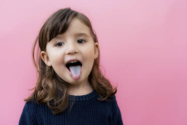 Portrait of little girl sticking out blue tongue in front of pink background - GEMF03493