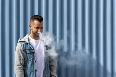 Young man smoking with an electronic cigarette over blue background - CAVF77186
