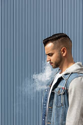 Young man smoking with an electronic cigarette over blue background - CAVF77187