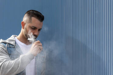 Young man smoking with an electronic cigarette over blue background - CAVF77189