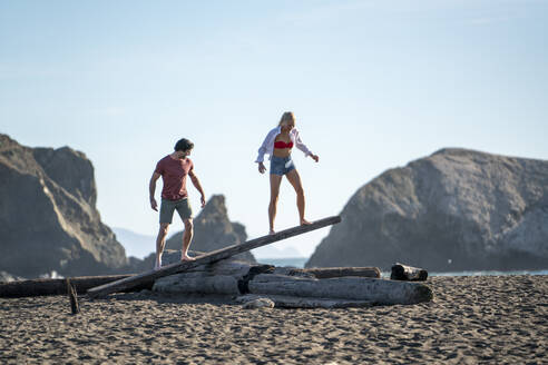Teenager-Paar balanciert auf Treibholz-Wippe am Strand - CAVF77238