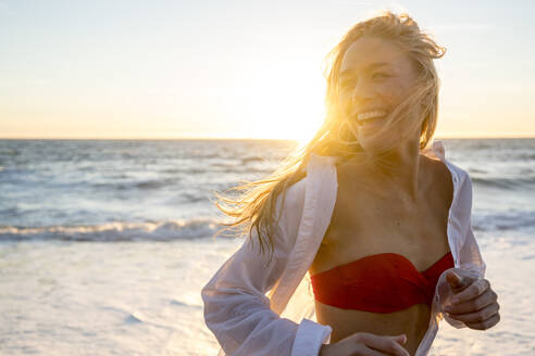 Teenage girl laughing as she runs on beach - CAVF77242