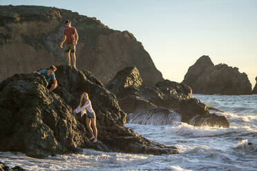 Group of teenagers hanging out on rocks at beach - CAVF77243