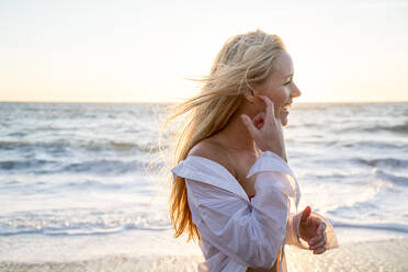 Teenage girl laughing on beach at sunset - CAVF77244