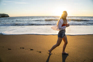 Teenage girl running on beach at sunset - CAVF77245