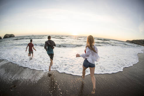 Gruppe von Teenagern, die sich bei Sonnenuntergang am Strand vergnügen - CAVF77246