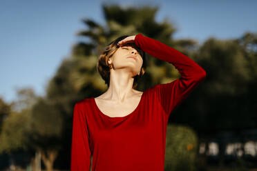 Porträt einer jungen Frau mit geschlossenen Augen in einem roten Kleid in einem Park - TCEF00250