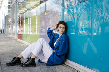 Young woman leaning on colorful glass wall with her reflection - TCEF00275