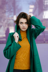 Junge Frau in grünem Mantel vor einer lila Glasscheibe - TCEF00287