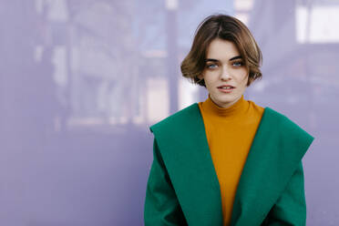 Junge Frau in grünem Mantel vor einer lila Glasscheibe - TCEF00288