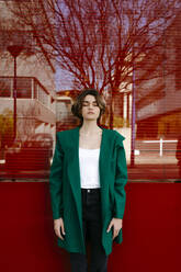 Junge Frau mit geschlossenen Augen und grünem Mantel vor einer Glasscheibe - TCEF00302