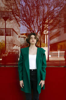 Junge Frau mit geschlossenen Augen und grünem Mantel vor einer Glasscheibe - TCEF00302