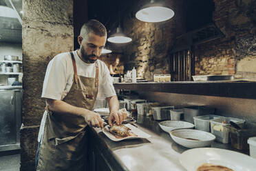 Chef arranging food on plate before serving in restaurant - MTBF00371