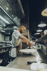 Chef arranging food on plate before serving in restaurant - MTBF00374