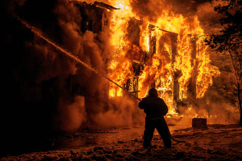 Feuerwehrmann sprüht Wasser auf brennendes Feuer in der Nacht - EYF01354