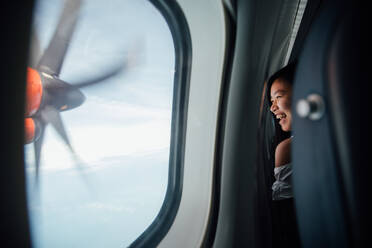 Glückliche junge Frau schaut durch das Fenster im Flugzeug - EYF01371