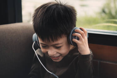 Netter lächelnder Junge hört Musik über Kopfhörer zu Hause - EYF01440