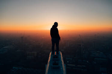 Rückansicht der Silhouette Mann Blick auf Stadtbild gegen den Himmel bei Sonnenuntergang - EYF01481