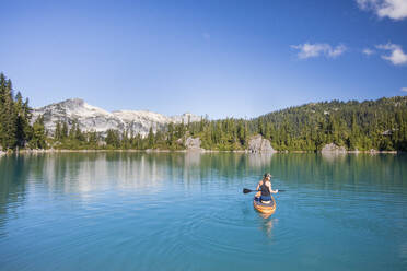 Aktive Frau paddelt Stand up Paddle Board auf blauem See. - CAVF77434