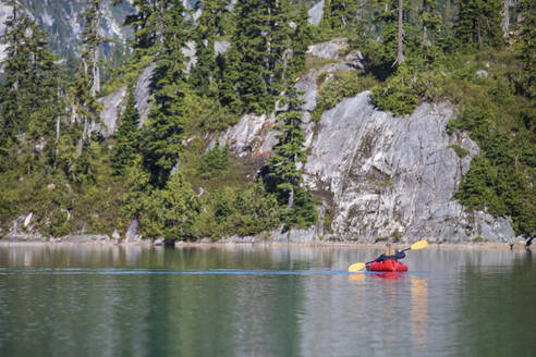 Rückansicht einer Rentnerin, die auf einem abgelegenen See mit einem Packraft paddelt. - CAVF77445