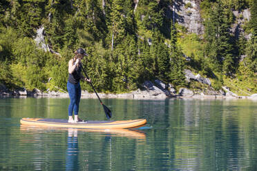 Young woman paddle boarding on remote lake. - CAVF77448