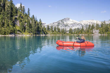 Eine Frau im Ruhestand paddelt mit einem roten Boot auf einem abgelegenen See während eines Ausflugs. - CAVF77456