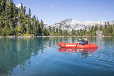 Retired woman paddling red boat on remote lake during a trip. - CAVF77456