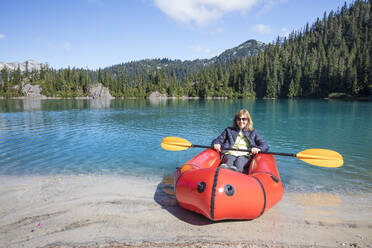 Retired woman enjoys paddling boat at remote lake. - CAVF77458