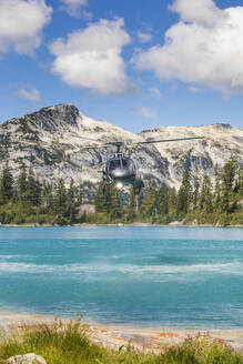 Helicopter flying low in mountains over alpine lake. - CAVF77480