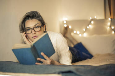 Young woman reads a book on a bed - CAVF77483
