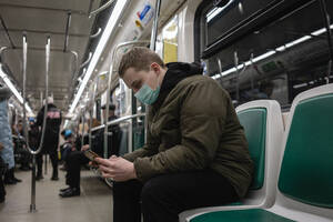Young man in commuter train, wearing face mask, using smartphone - VPIF02132
