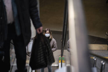 Woman with face mask on escalator at railway station - VPIF02136
