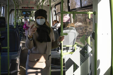 Frau mit Gesichtsmaske benutzt Smartphone in der Straßenbahn - VPIF02140