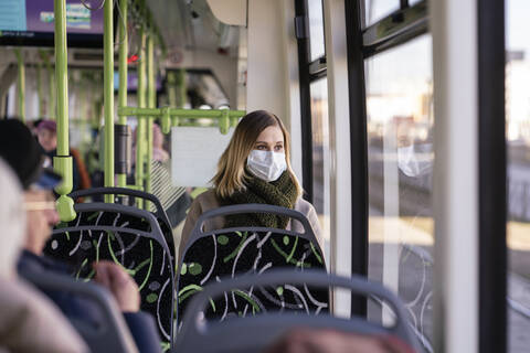 Frau mit Gesichtsmaske in Straßenbahn sitzend, lizenzfreies Stockfoto