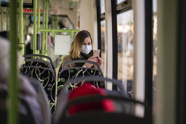 Woman with face mask sitting in tram, using smartphone - VPIF02142