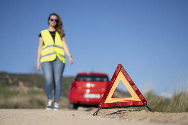 Warndreieck vor einem kaputten Auto auf einer Landstraße, lizenzfreies  Stockfoto