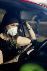 Woman in car wearing respirator mask using cell phone - OCMF01081