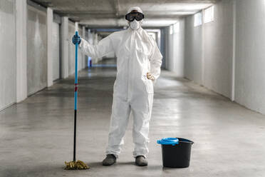 Woman wearing protective clothing wiping floor of car park - DLTSF00649