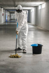 Woman wearing protective clothing wiping floor of car park - DLTSF00650